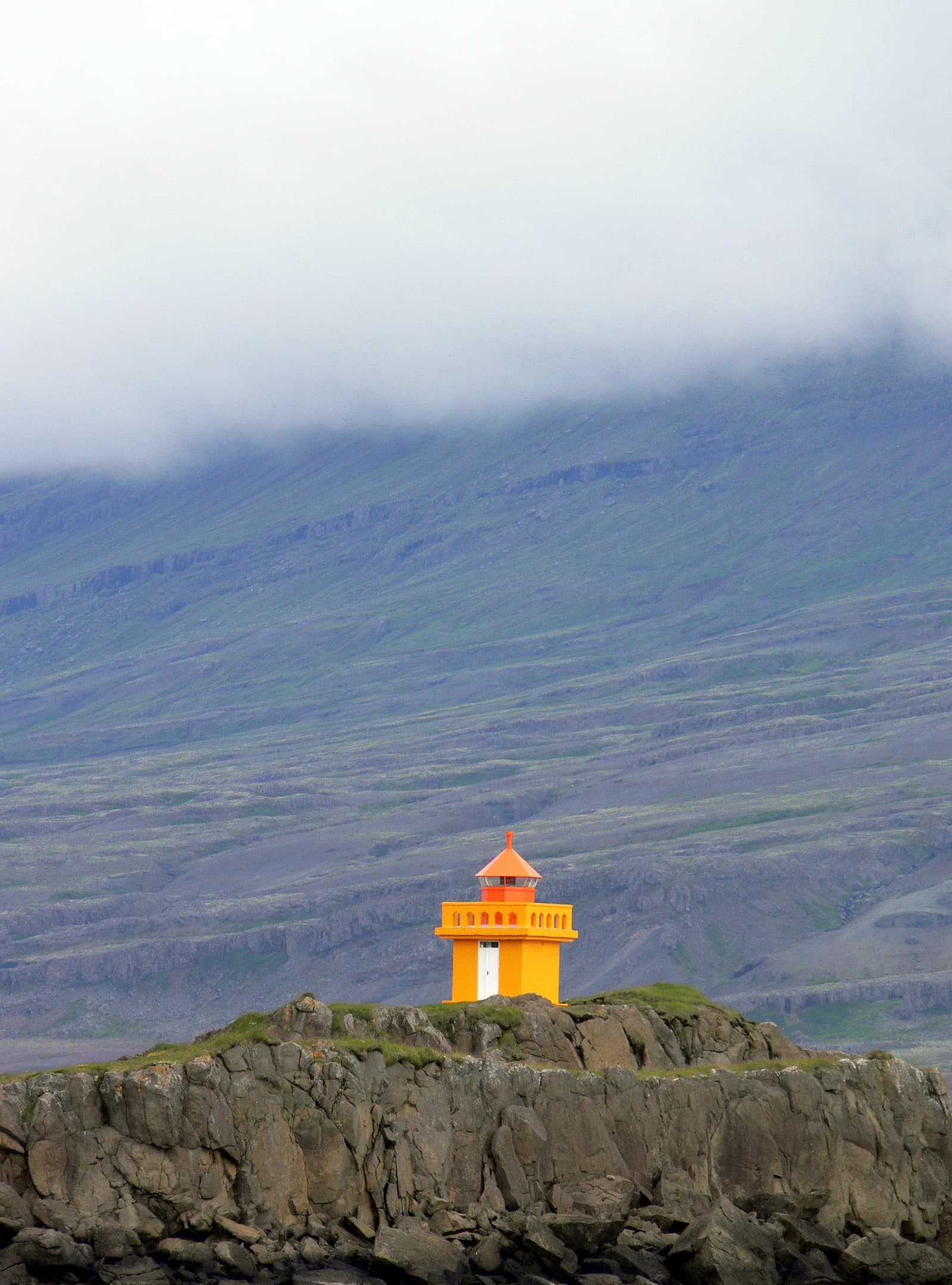 Orange Djúpivogur Lighthouse standing above the East Iceland shoreline.