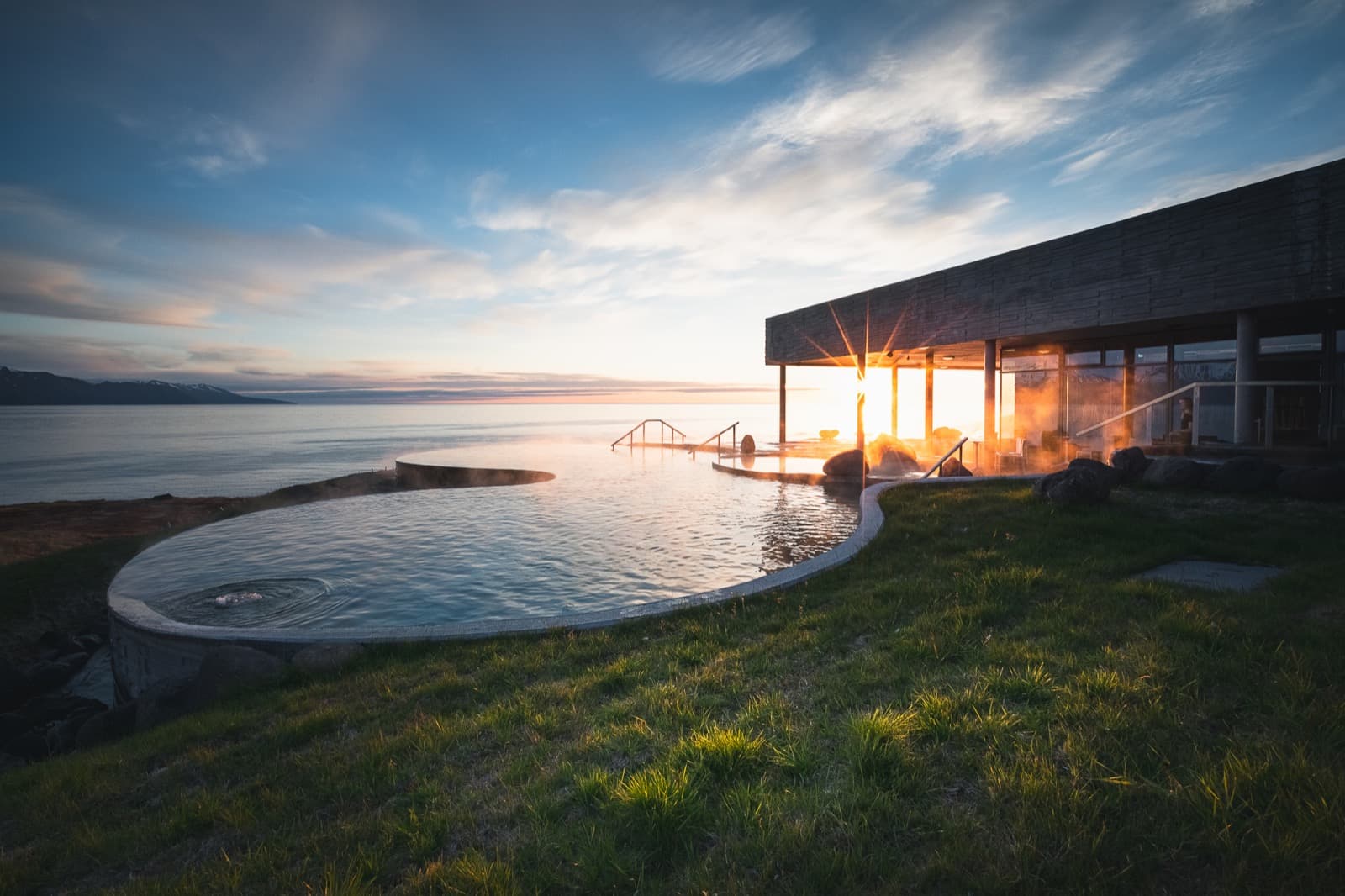 Steam rising from GeoSea's outdoor pools beside the bathhouse and Skjálfandi Bay at low sun.