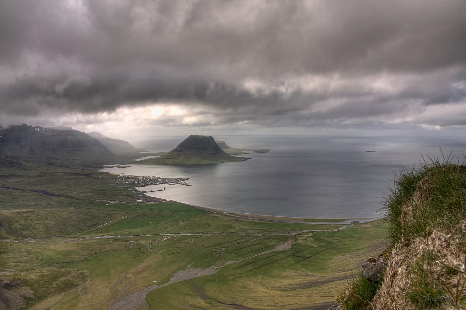 High overlook above Grundarfjörður showing the town, fjord, and Kirkjufell under dark cloud.