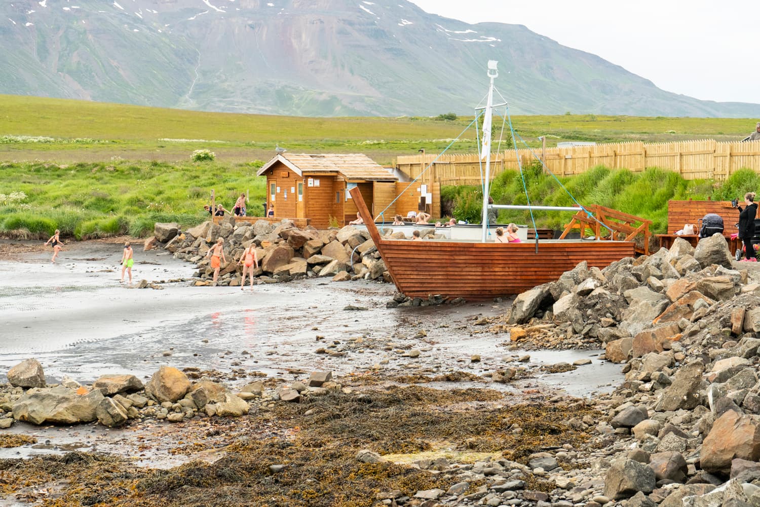 Boat-shaped bath and black-beach shoreline at Hauganes with mountains behind