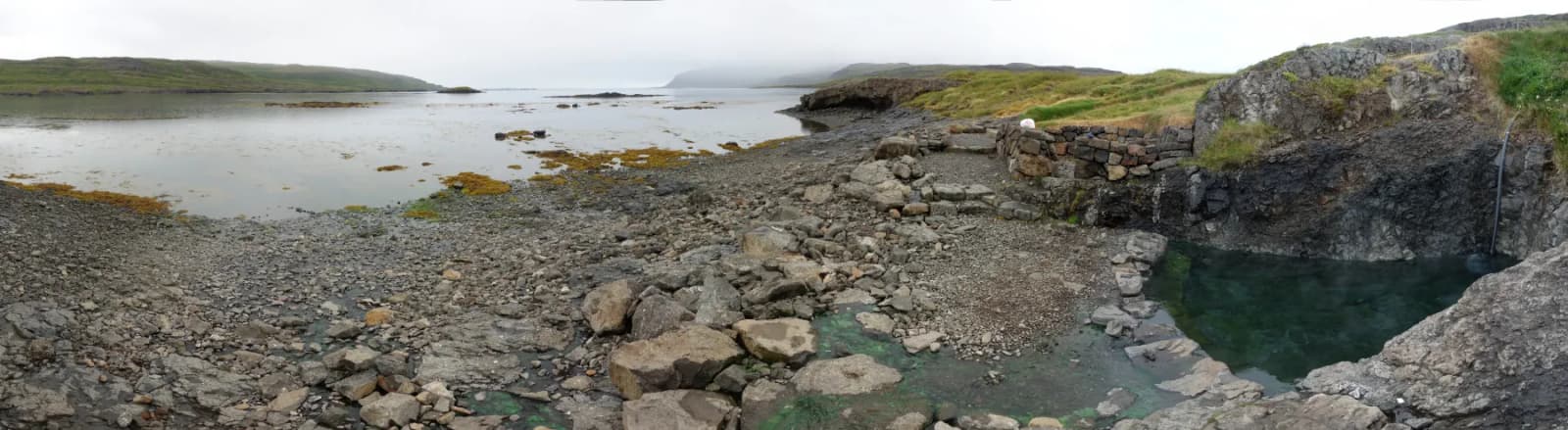 Wide panorama of Hellulaug hot pool and the Vatnsfjörður shoreline.