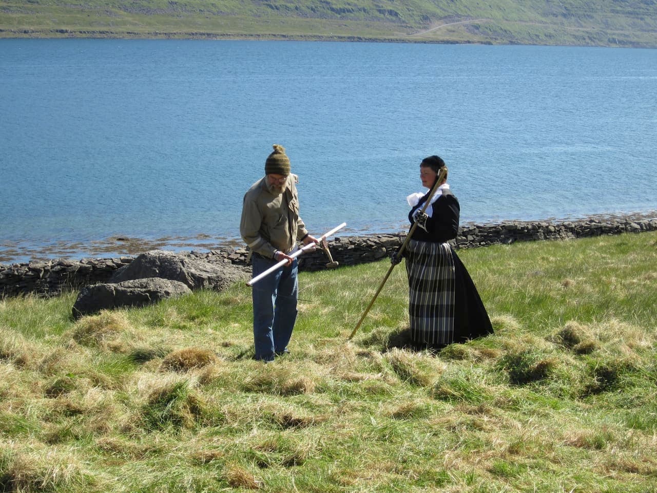People in traditional clothing on the grass near Litlibær with Skötufjörður water behind them.