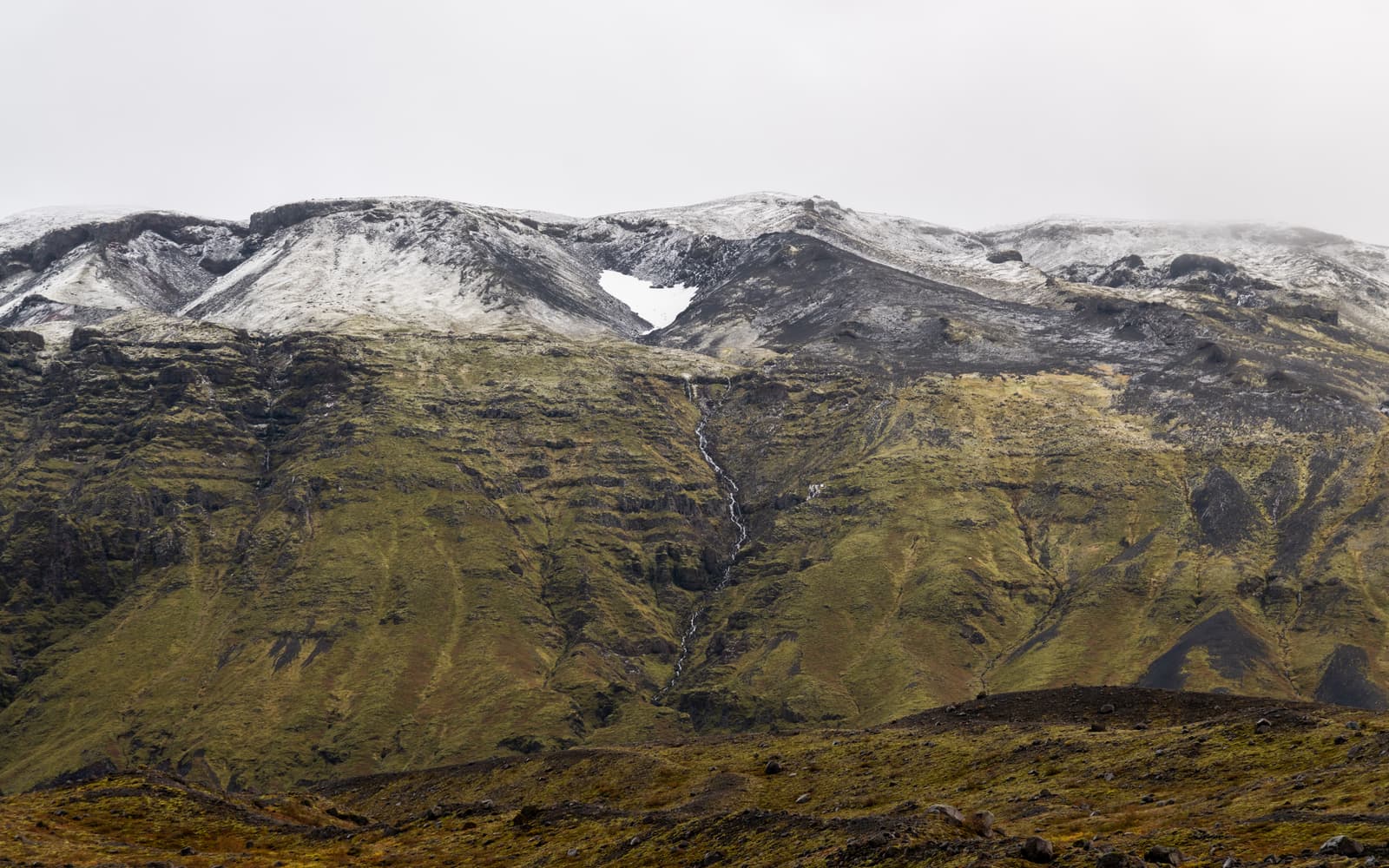 A narrow waterfall dropping below a snow patch in Skaftafell National Park.