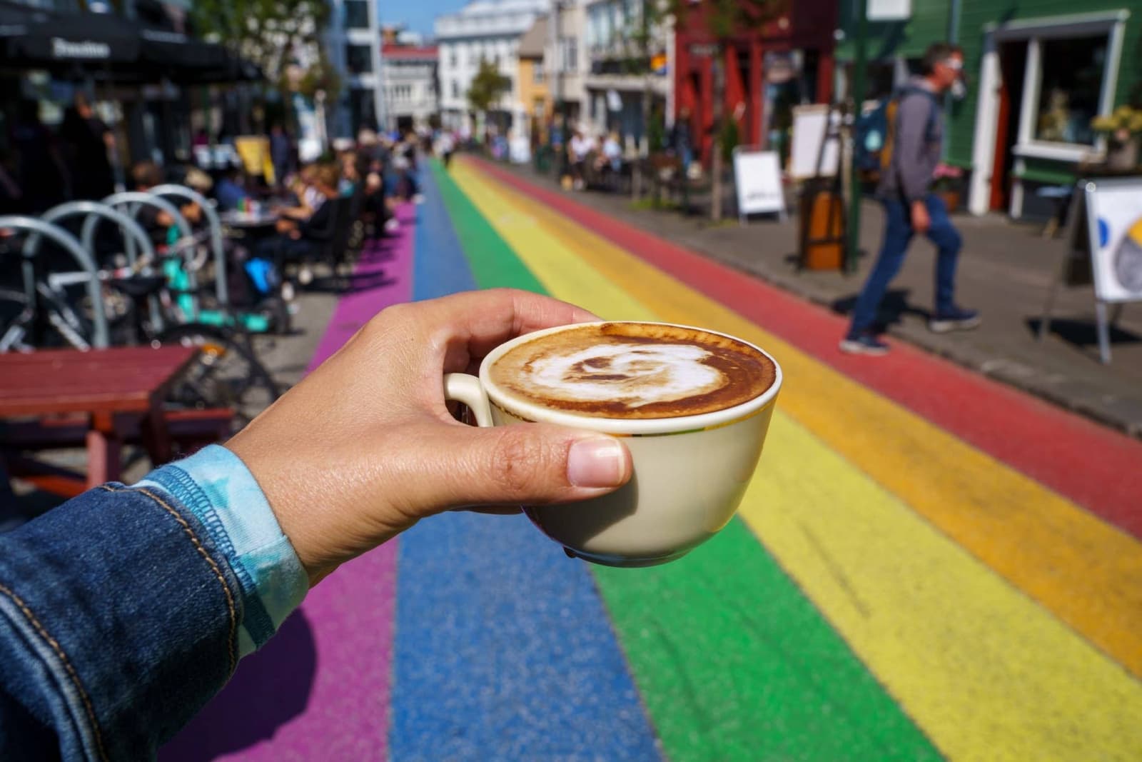 A coffee cup held above the rainbow pavement of Skólavörðustígur in Reykjavík.