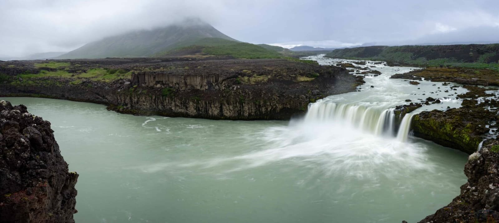 Þjófafoss waterfall on Þjórsá with snowy Hekla visible beyond dark lava fields.