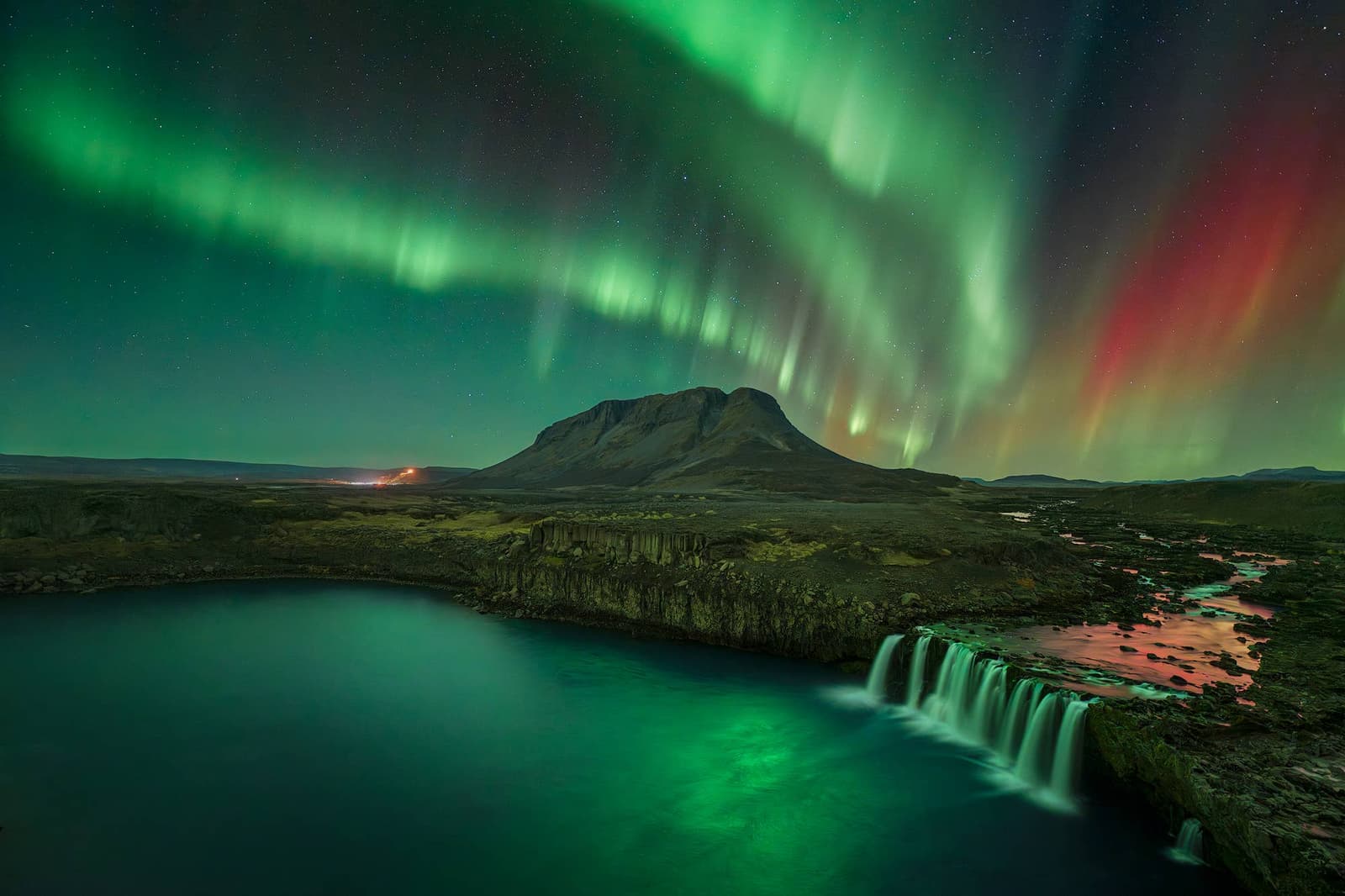 Þjófafoss waterfall below a dark sky with northern lights over the Hekla area.