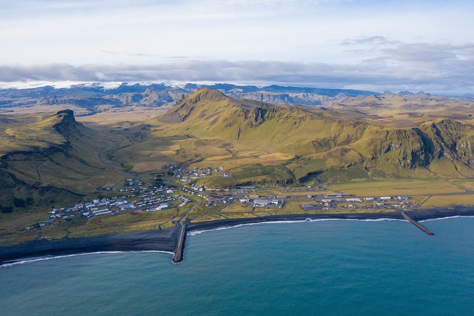 Aerial view of Vík showing the village, black-sand shore, and steep South Coast slopes.