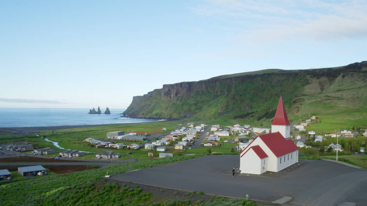 Vík village, church, black-sand coast, and Reynisdrangar seen together from above town.