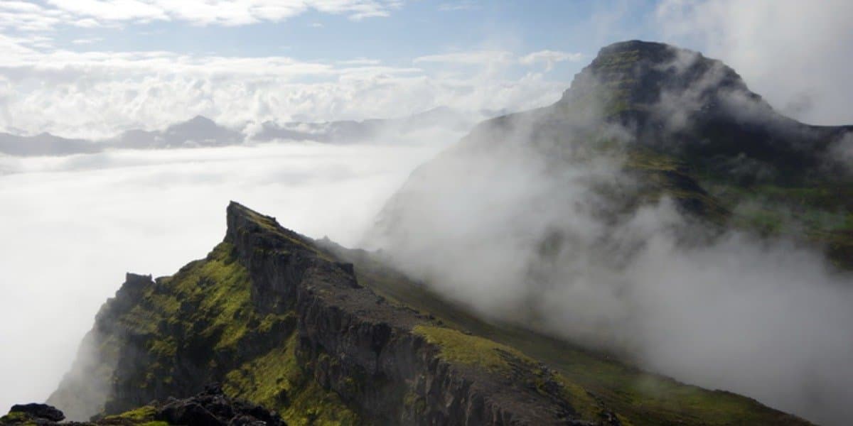 People walking the track across grassy ground below steep slopes on the Vöðlavík side of the Eastfjords.