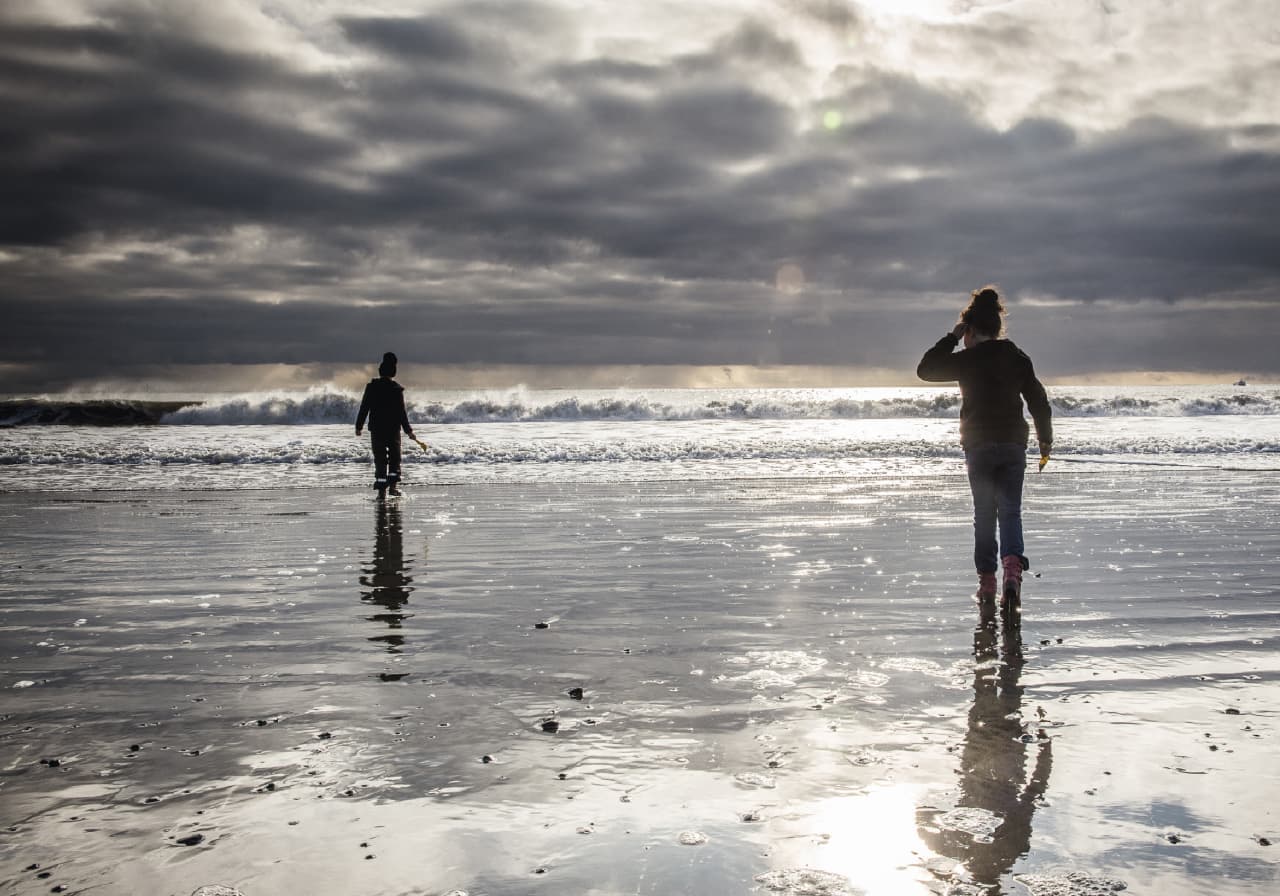 People walking on Langisandur beach in Akranes with low surf and mountains in the distance.