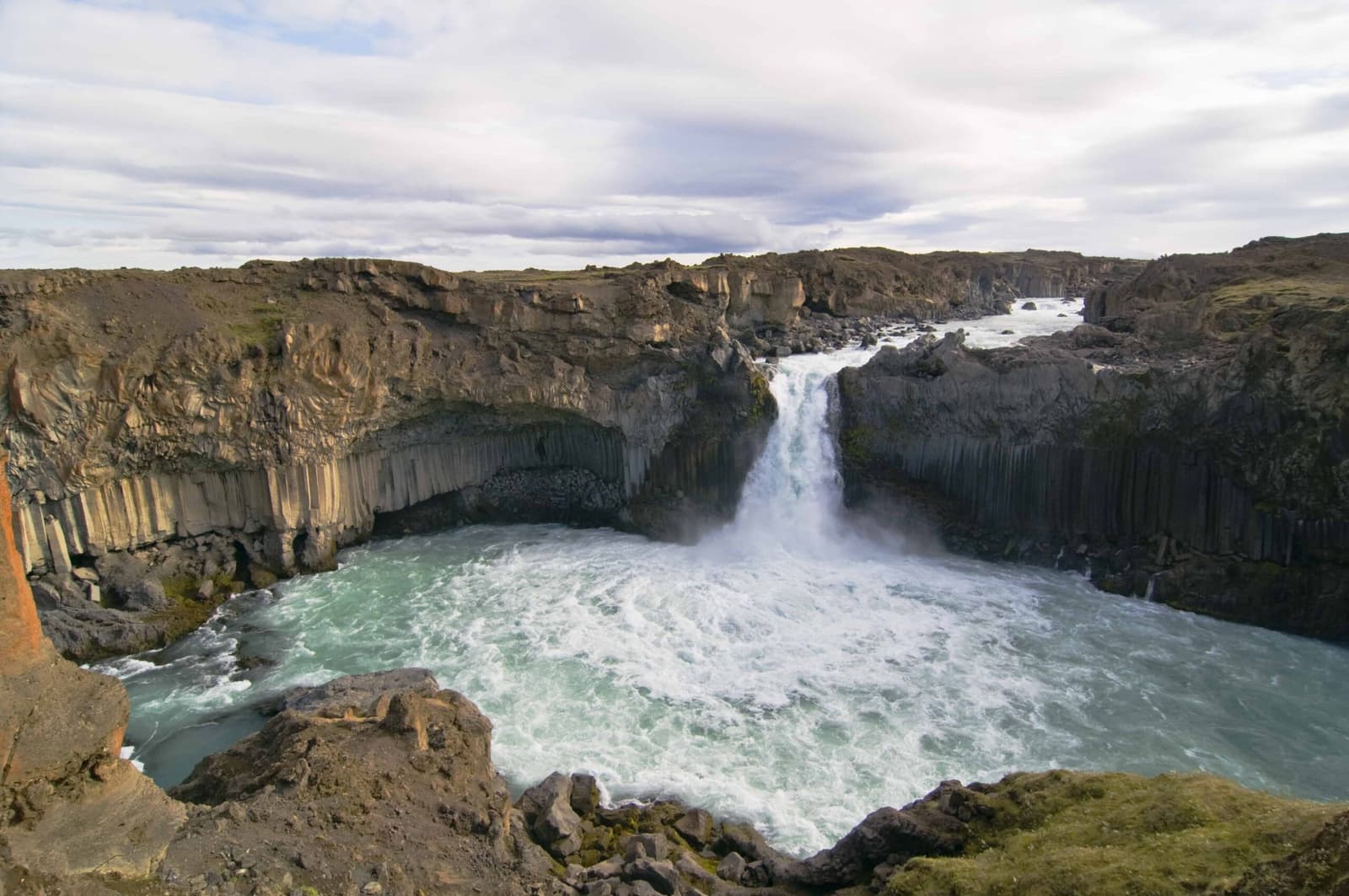 Aldeyjarfoss dropping into a pale river pool below dark basalt columns in North Iceland.