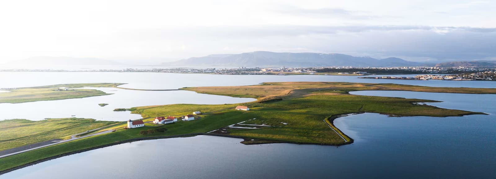 Aerial view of Álftanes with ponds, shoreline, Bessastaðir, and Reykjavík across the water.