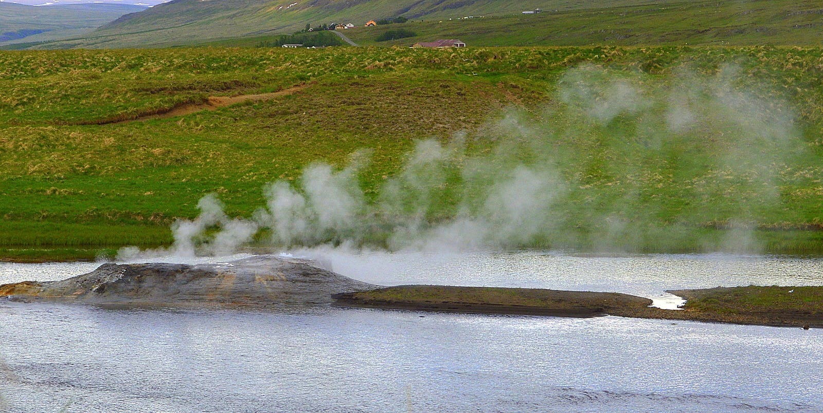 Steam rising from Árhver hot spring in the Reykjadalsá river during green summer conditions near Reykholt.