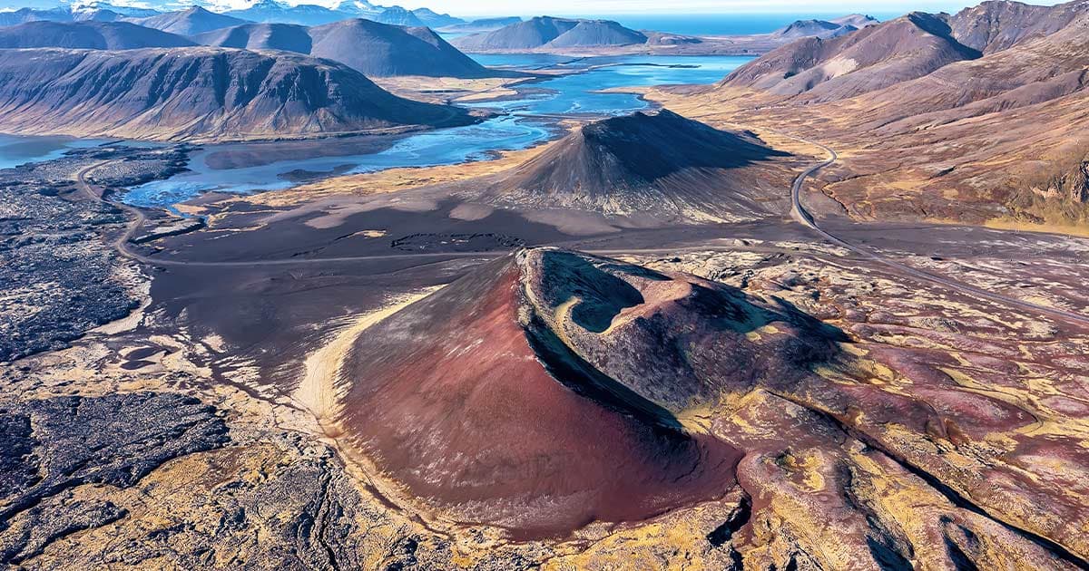 Red crater and dark lava field at Berserkjahraun with Snæfellsnes mountains and water beyond.