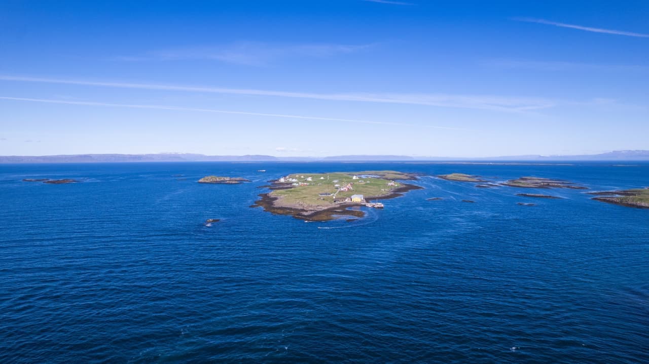 Flatey island village, low green land, and blue Breiðafjörður water seen from above.
