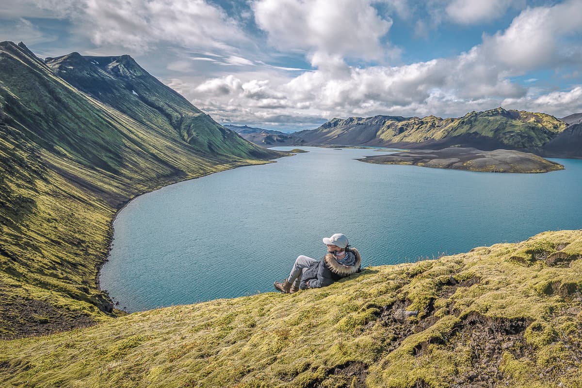High view from the Breiðbakur area over Langisjór lake, mossy ridges, dark highland slopes, and a seated traveler.