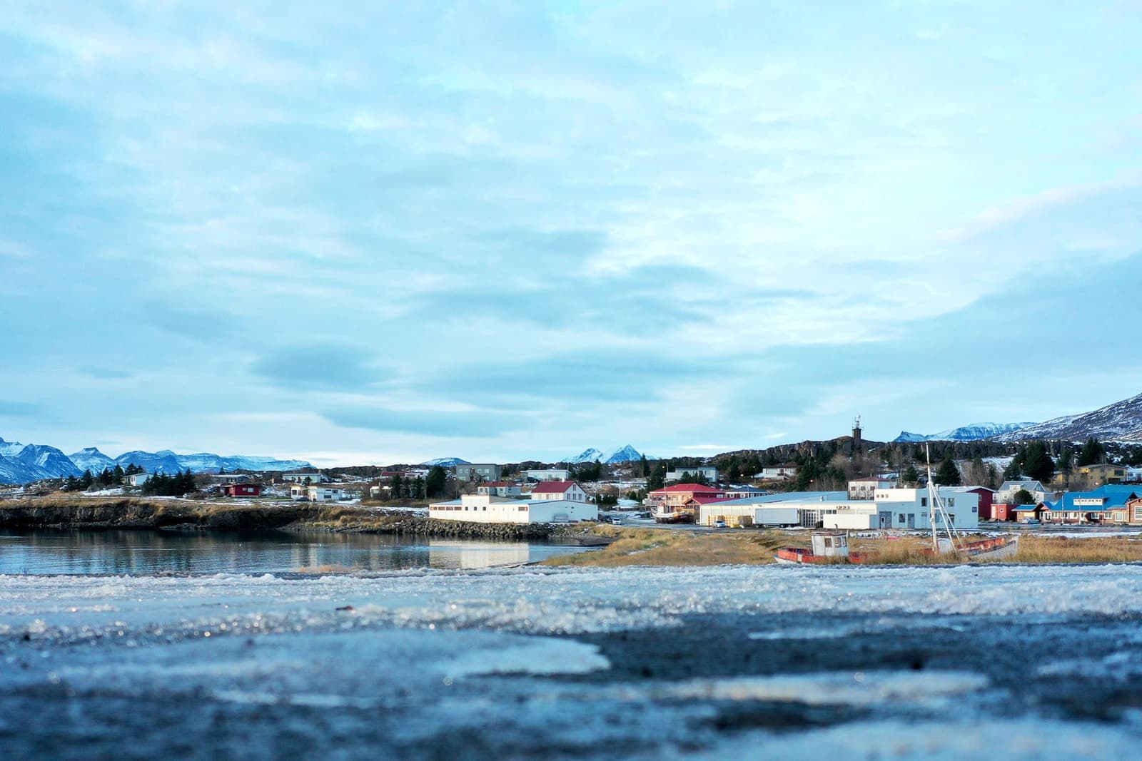 Breiðdalsvík village beside the bay with low buildings, mountains, and snow-edged shoreline in East Iceland.