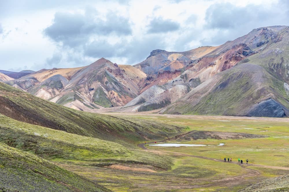 Hikers on a trail below colorful rhyolite slopes near Brennisteinsalda in Landmannalaugar.