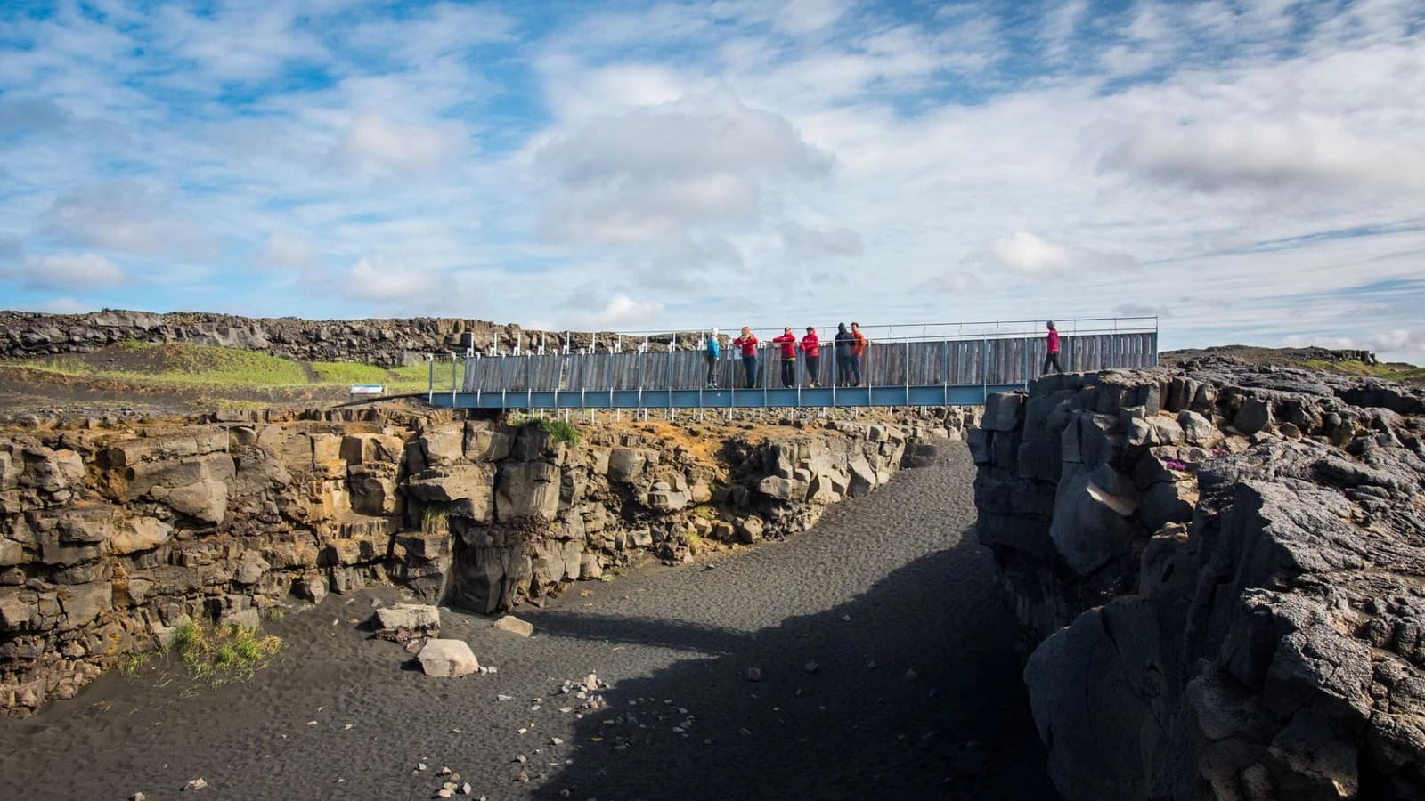 Bridge Between Continents crossing a dark volcanic fissure on the Reykjanes Peninsula.