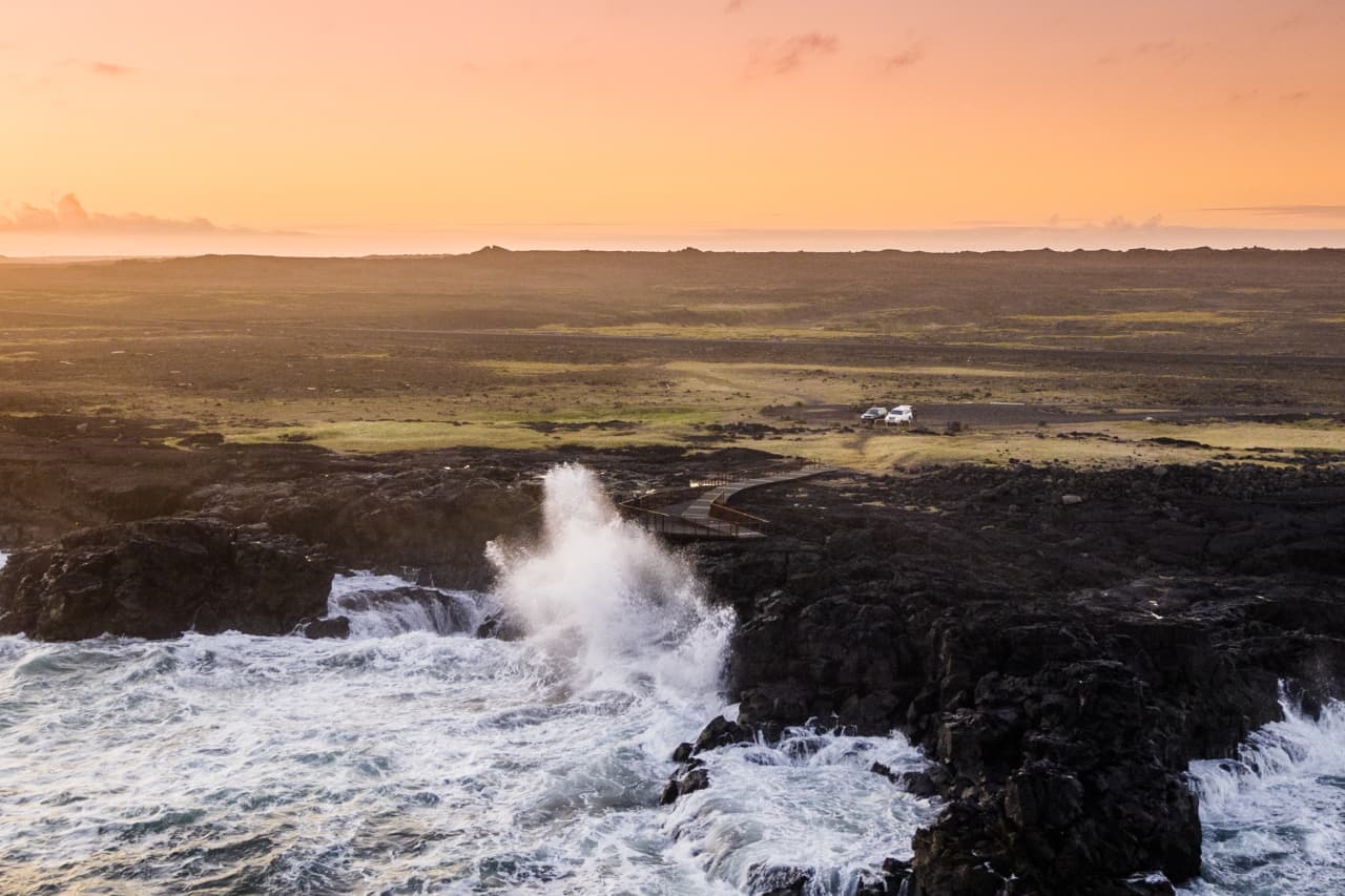 Sunset light over Brimketill as waves strike the black lava shore below the viewing platform.