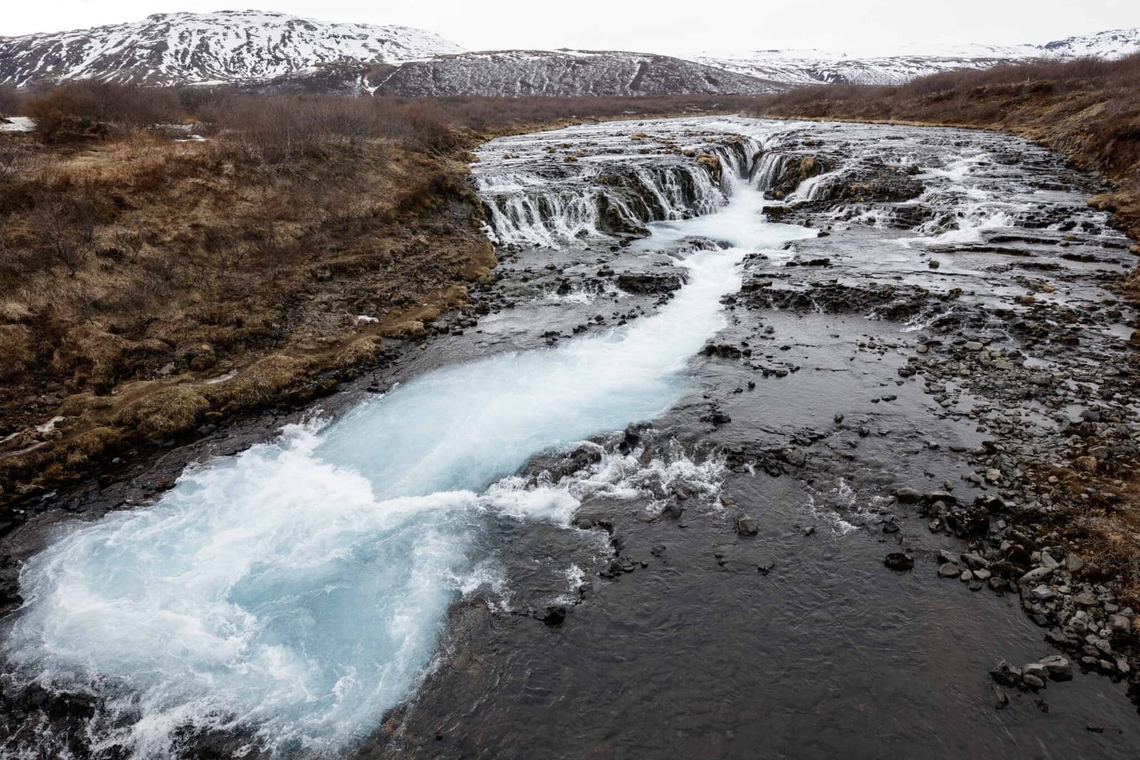 Wide view of Brúará flowing through dark rock and low Brúarfoss cascades in South Iceland.