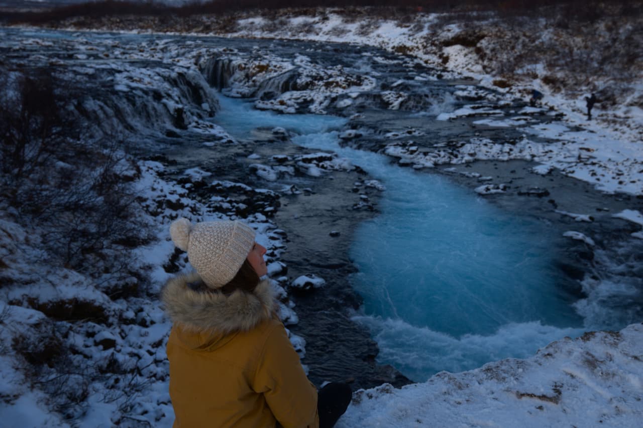 Visitor beside the blue Brúará river channel and low Brúarfoss cascades in winter.
