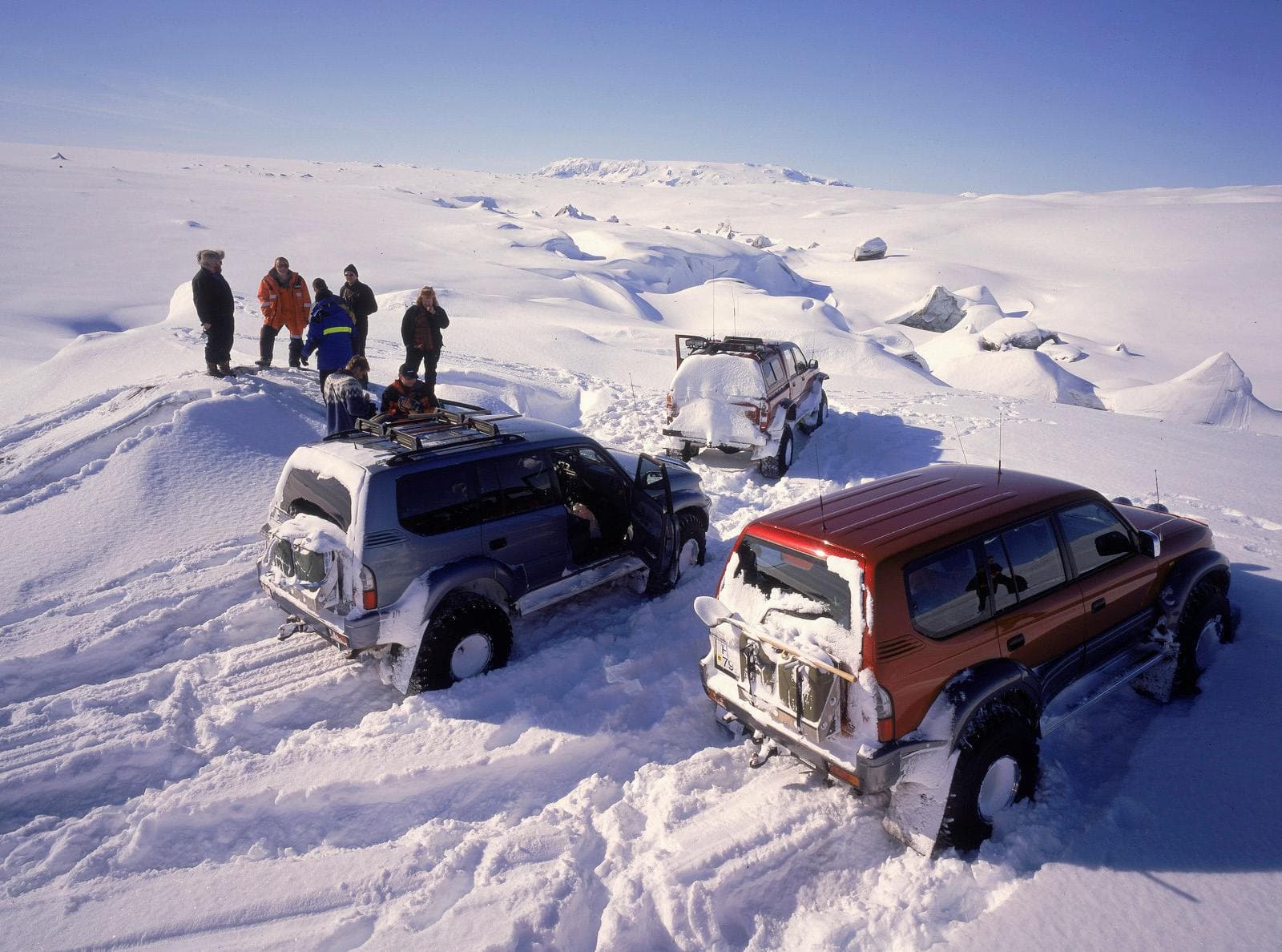 Super jeeps and travelers parked on deep snow beside the Brúarjökull glacier landscape.