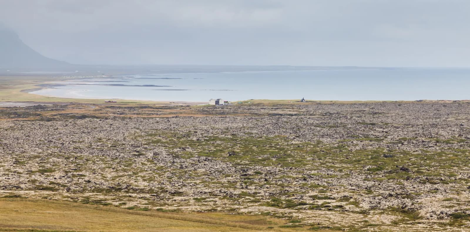 Búðahraun lava field, pale sand, mossy lava, Búðakirkja, and Snæfellsnes mountains near Búðir.