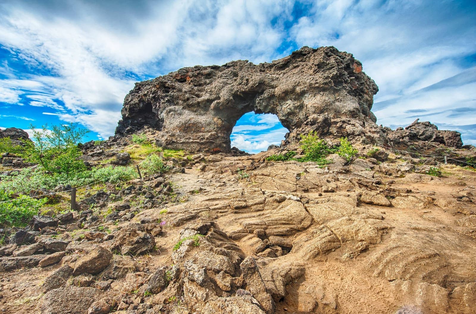 Dimmuborgir lava arch rising from rough volcanic rock under a bright North Iceland sky.