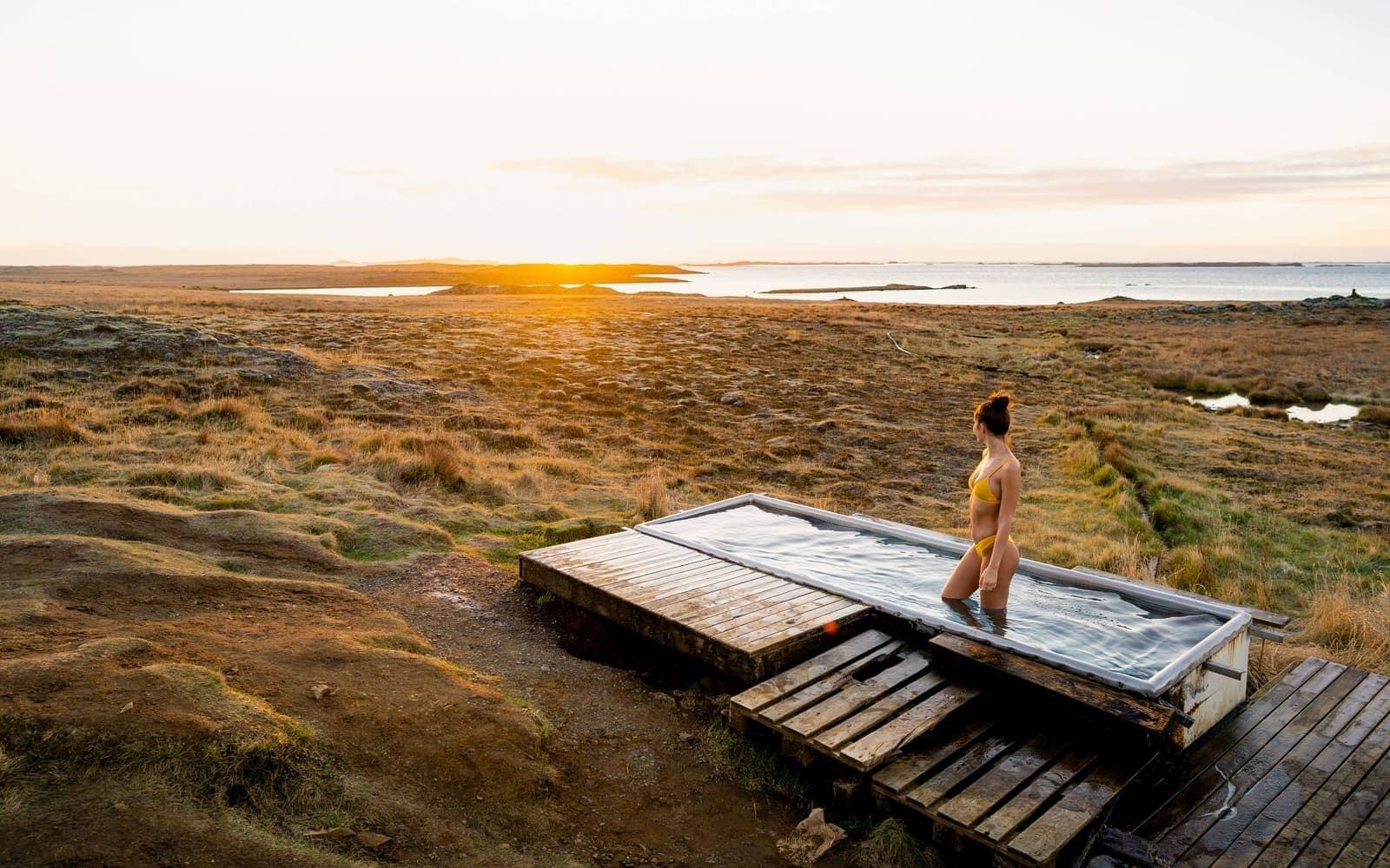 Small Djúpavogskörin hot spring tub and wooden deck in open East Iceland grassland at sunrise.