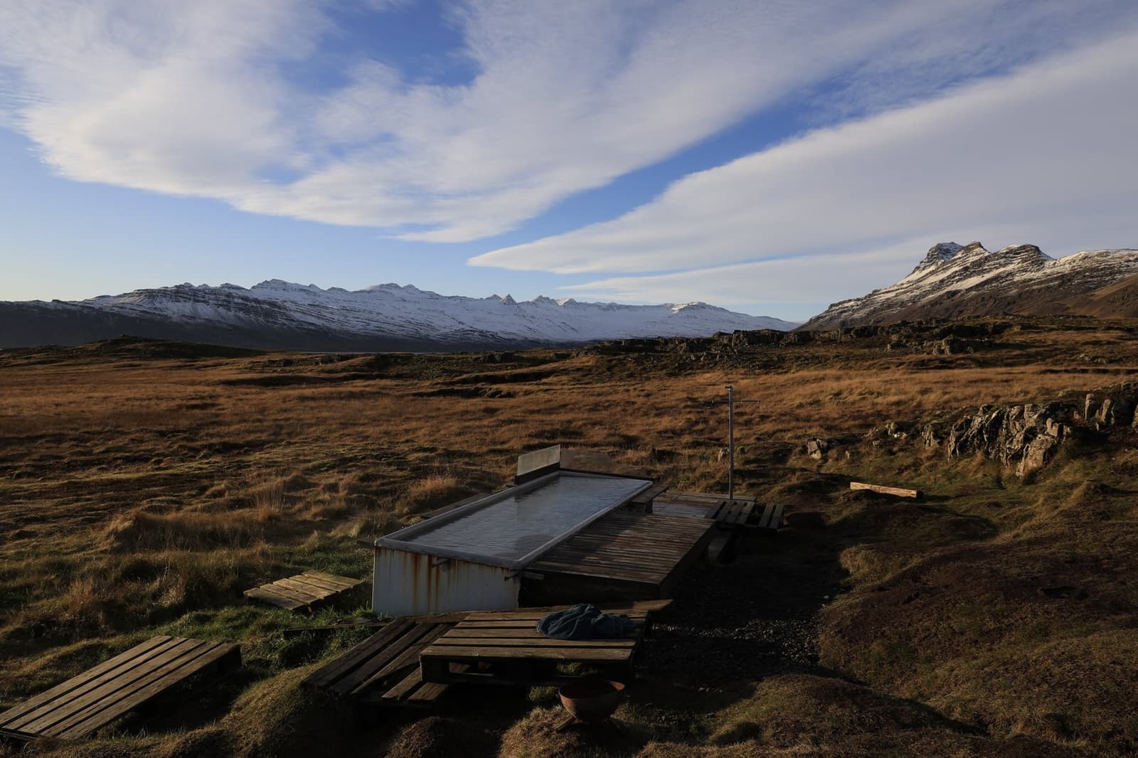 Wide view of Djúpavogskörin hot spring below rocks with open East Iceland mountains beyond.