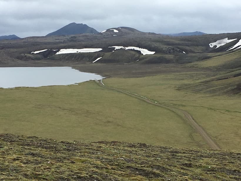 Dómadalsvatn lake and a rough track across the green Dómadalur valley floor below dark Highland hills.