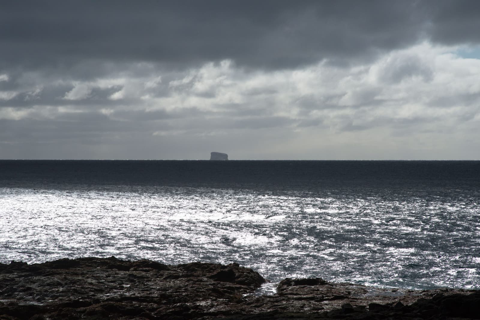Eldey visible as a dark offshore island beyond rough Reykjanes lava and bright sea.