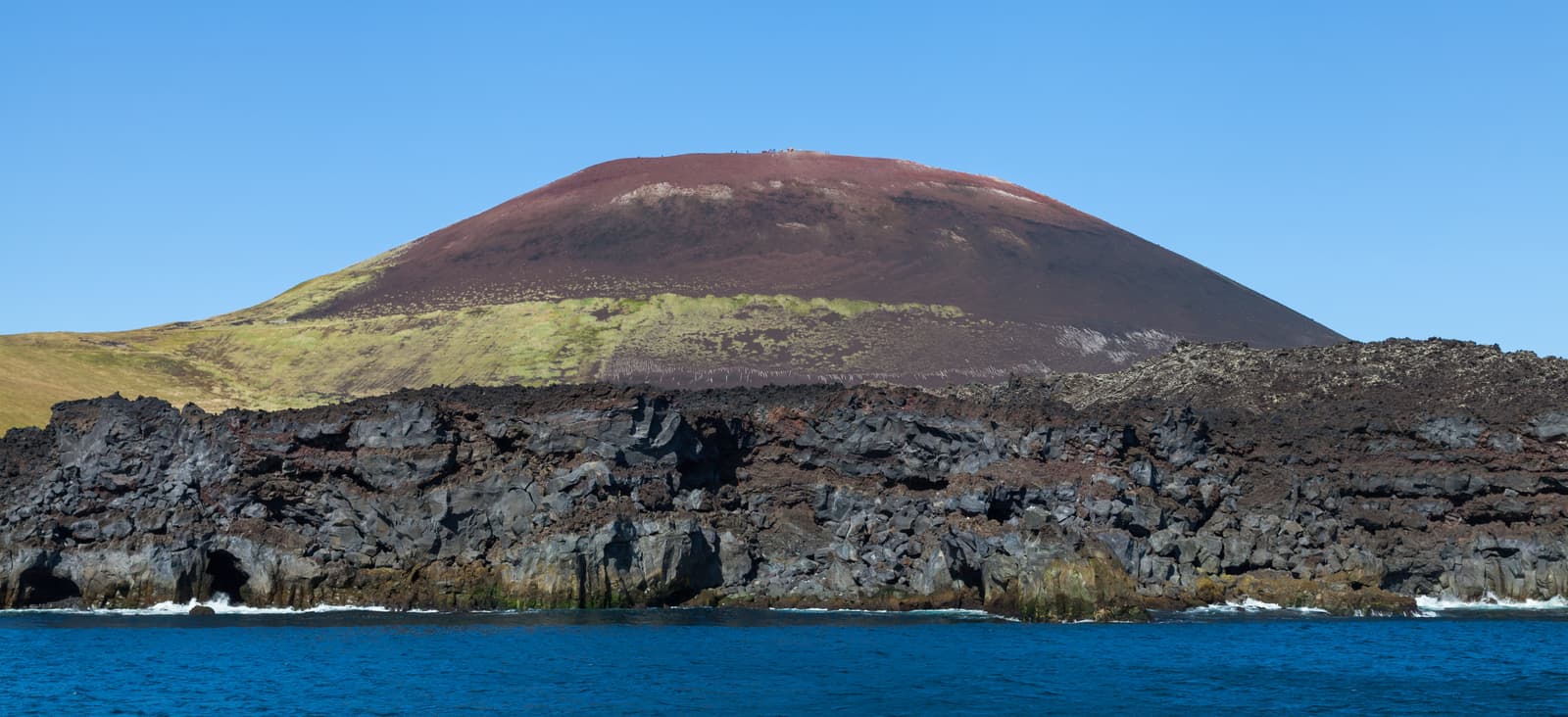 Eldfell's red volcanic crater slopes on Heimaey with tiny hikers along the ridge.