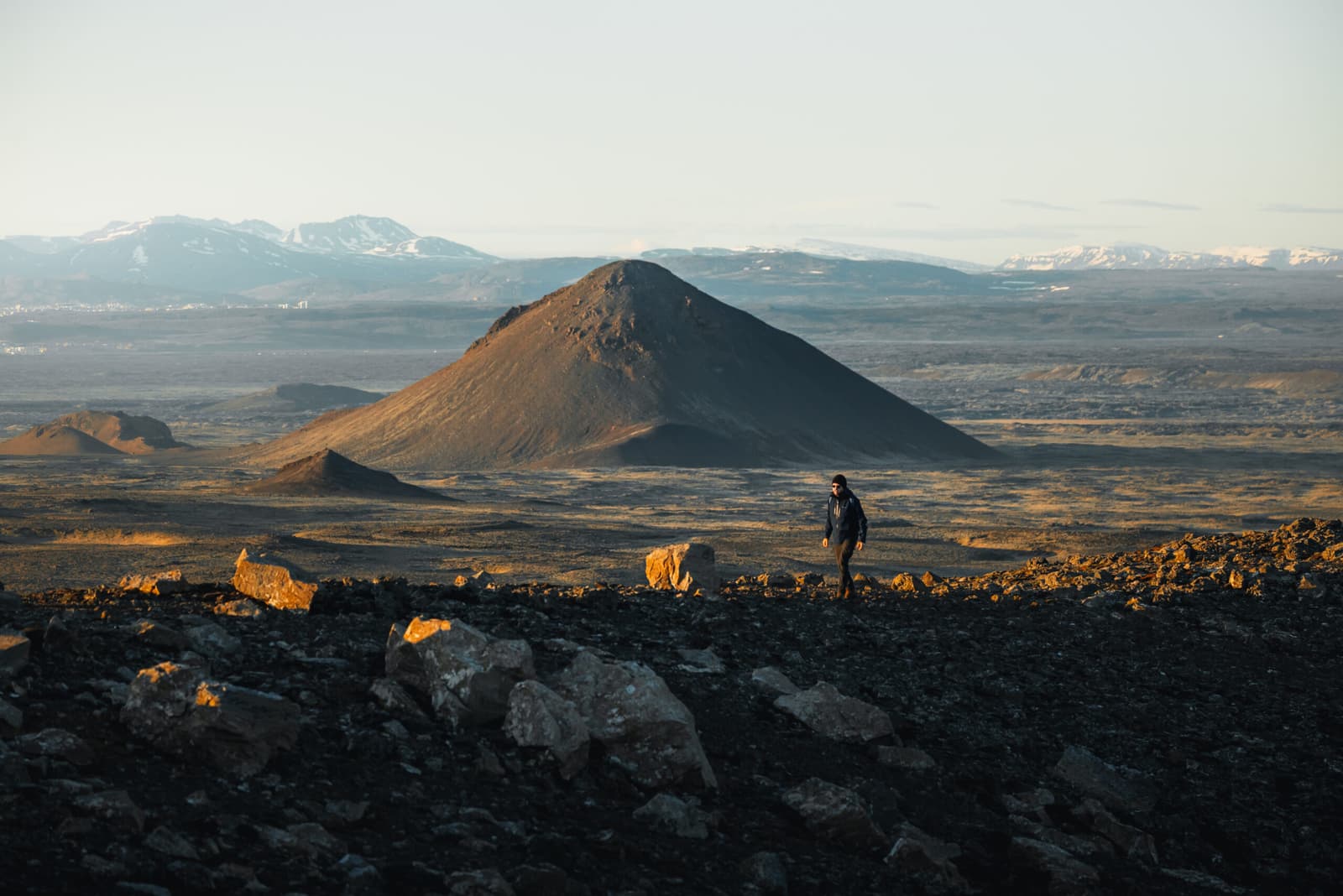 Hiker above a dark Fagradalsfjall cone and lava fields on the Reykjanes Peninsula.