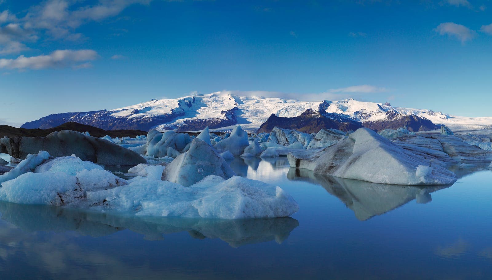 Icebergs in Fjallsárlón with Fjallsjökull glacier and snowy mountains behind them.