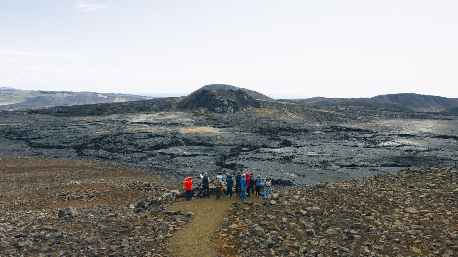 Hikers above the cooled lava and broad eruption valley of Geldingadalur on Reykjanes.