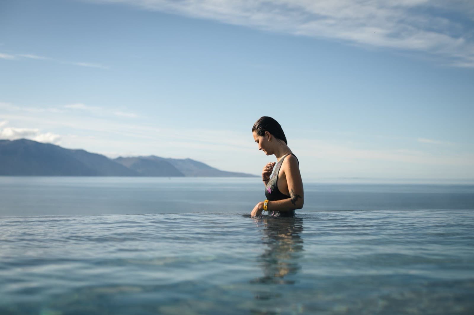 Swimmer in GeoSea's cliffside pool with Skjálfandi Bay and mountains beyond Húsavík.