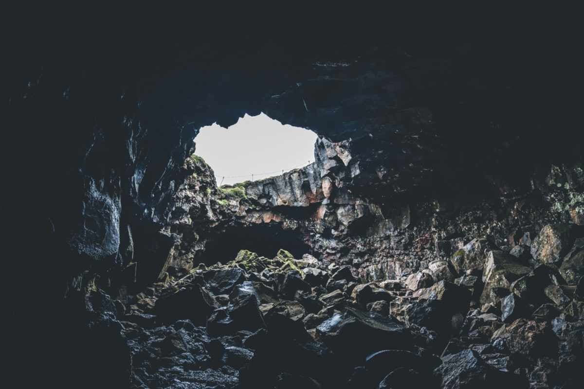 Dark Gjábakkahellir cave opening with loose lava rocks on the floor and daylight at the entrance.