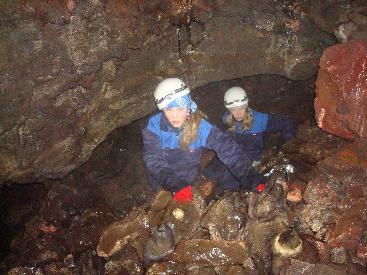 Helmeted visitors moving through a low rocky section of Gjábakkahellir cave.