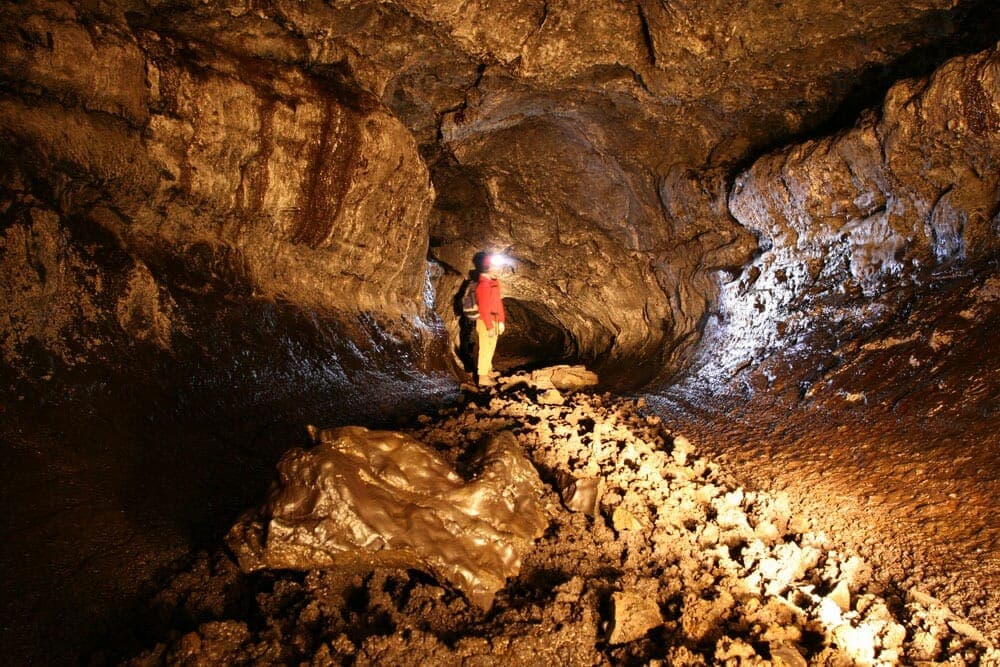 A helmeted visitor with a headlamp standing on loose rock inside Gjábakkahellir lava tube.
