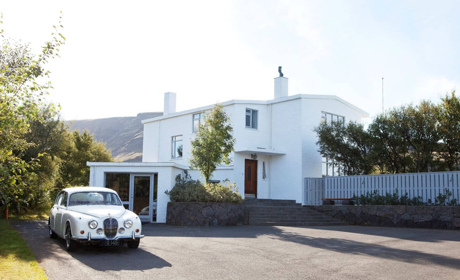 The white Gljúfrasteinn house museum in Mosfellsdalur with a vintage car outside.