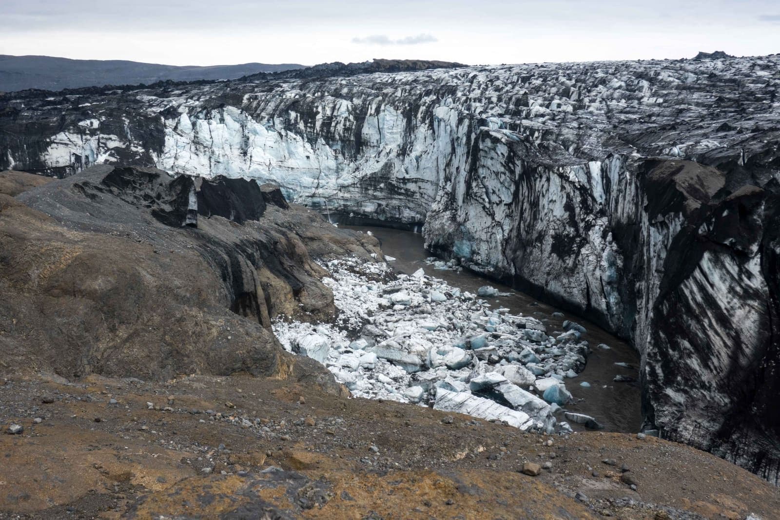 Broken glacier ice and a silty drainage trench at Grænalón below the dark mountains of southeast Iceland.