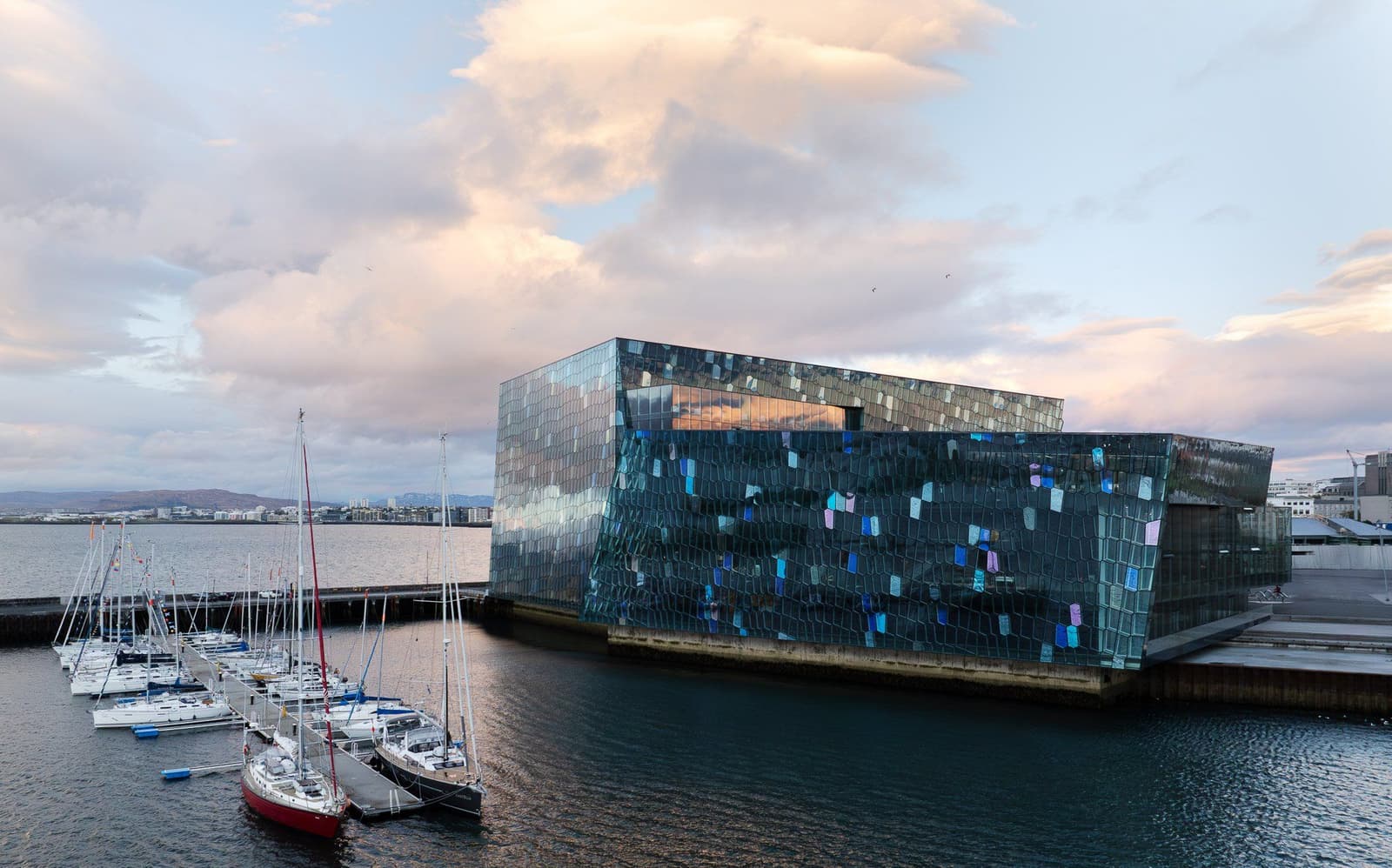 Harpa Concert Hall on Reykjavík waterfront with glass facade, harbor boats, and Faxaflói Bay