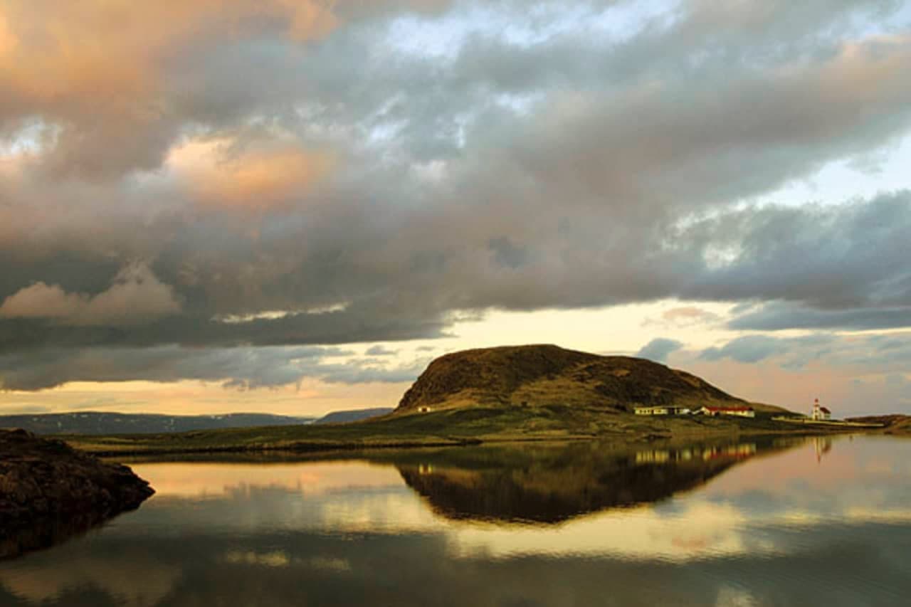 Helgafell reflected in still water with Helgafell church at the base of the mountain.
