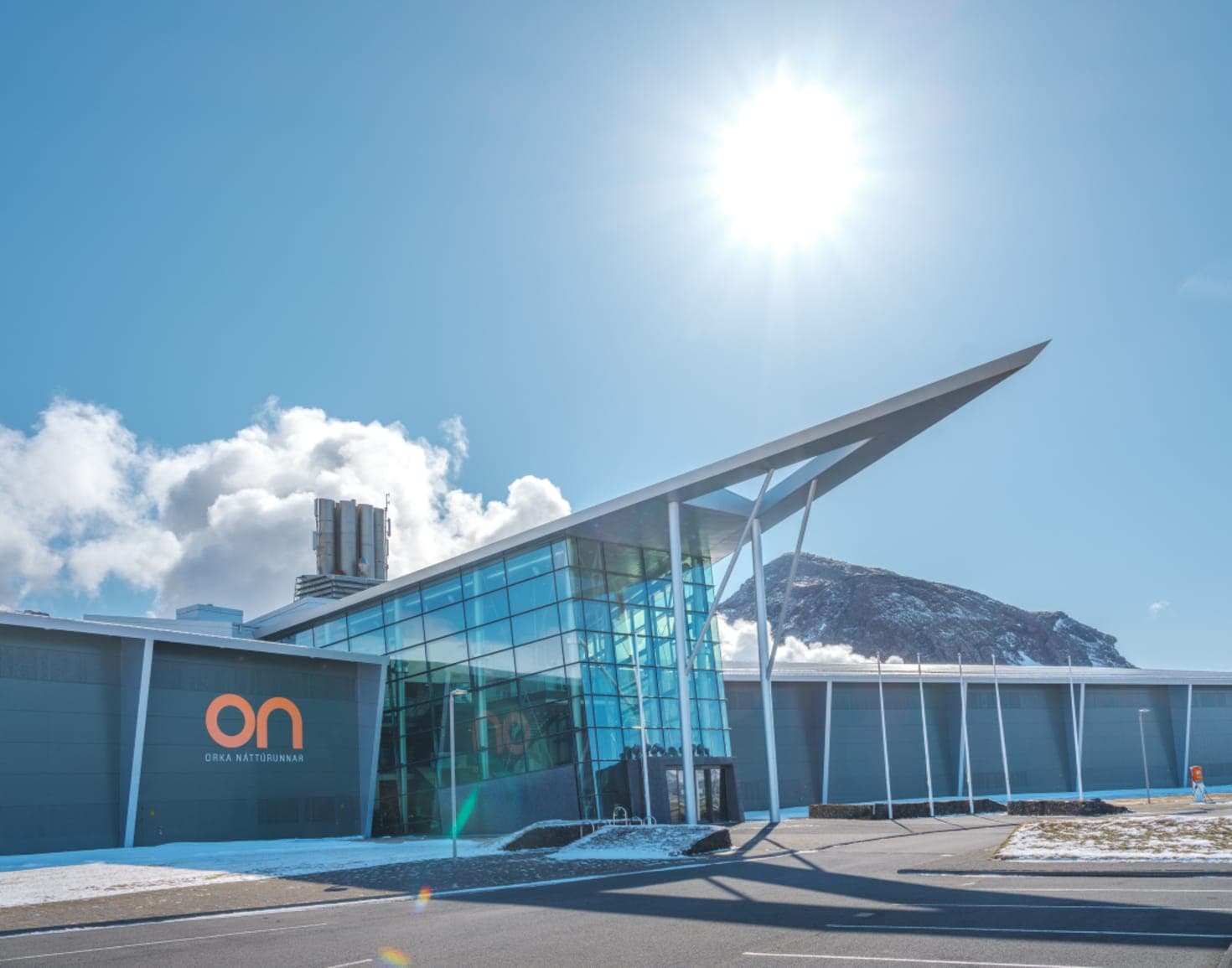Hellisheiði Geothermal Exhibition building with steam rising behind it and snowy mountains beyond.