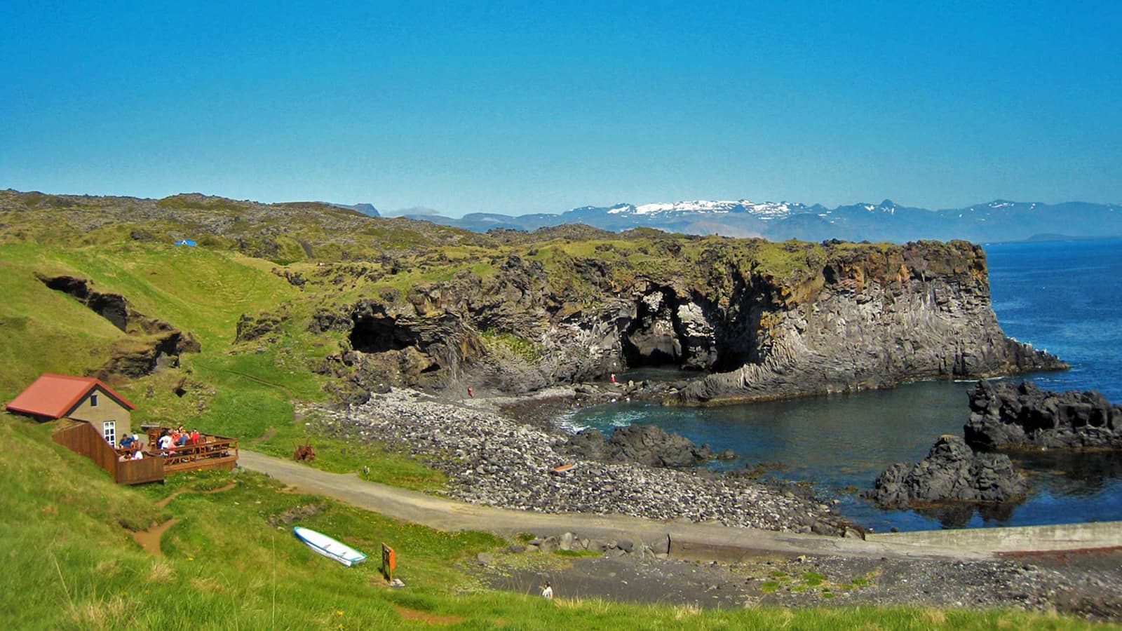 Hellnar shoreline with black lava cliffs, a small seafront building, and the Atlantic below Snæfellsnes.