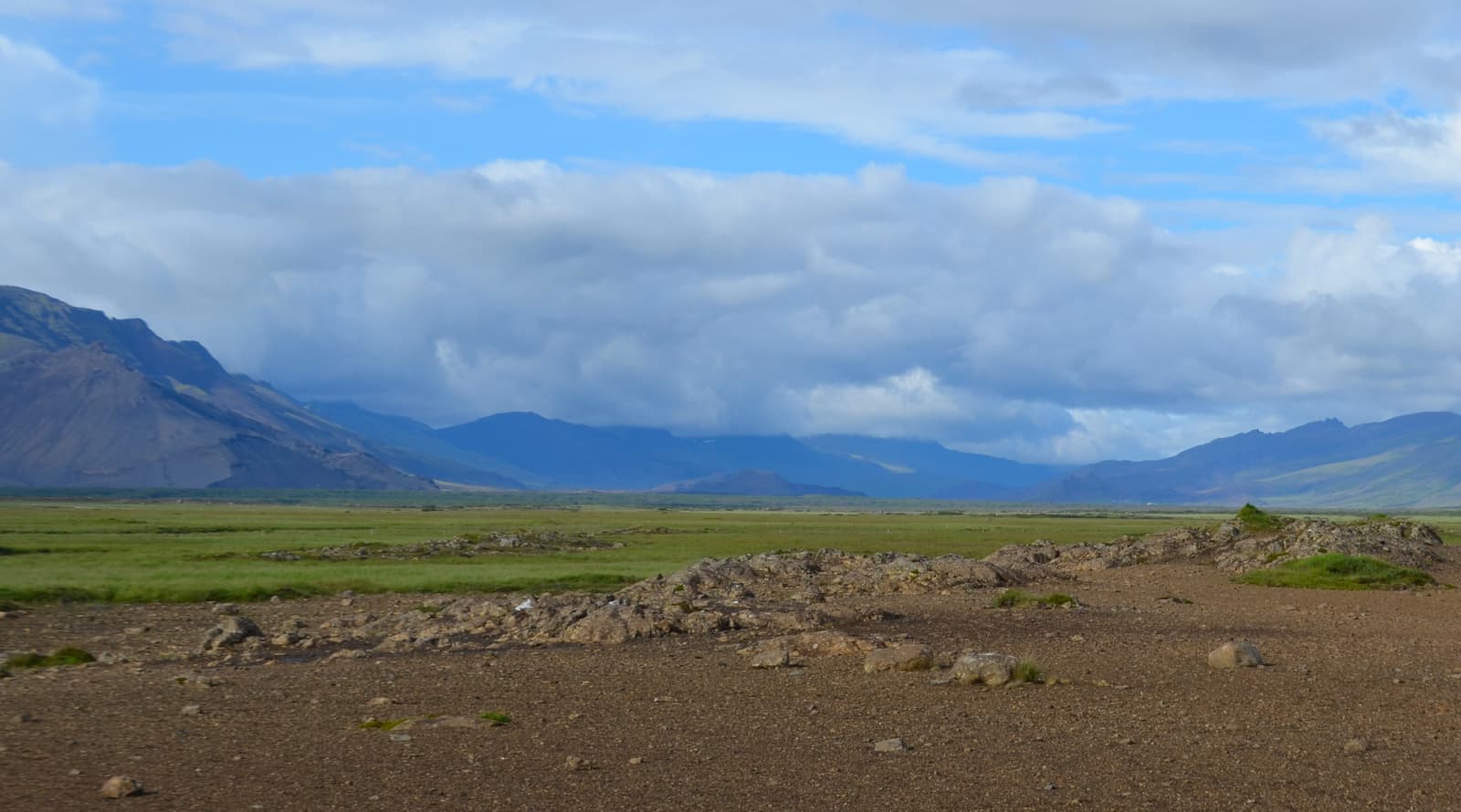 Wide view across Hítardalur valley with lava ground, green lowland, mountains, and clouds in West Iceland.