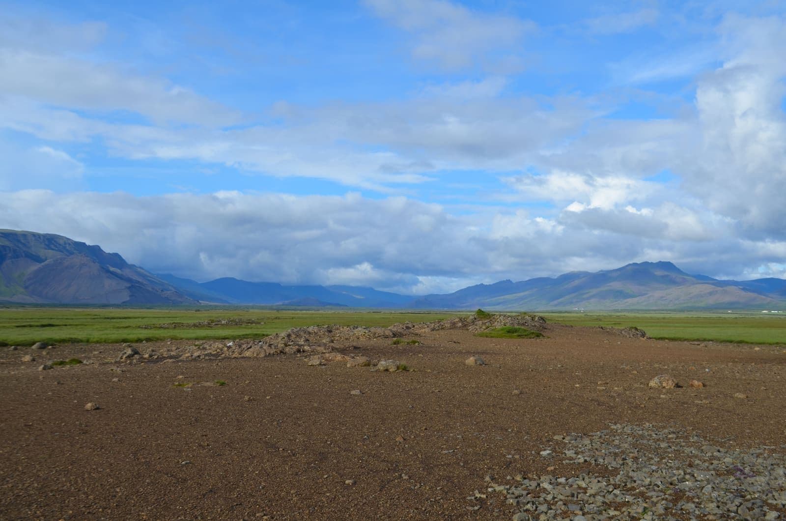 Hítardalur valley with lava foreground, green lowland, mountains, and a large cloudy sky.
