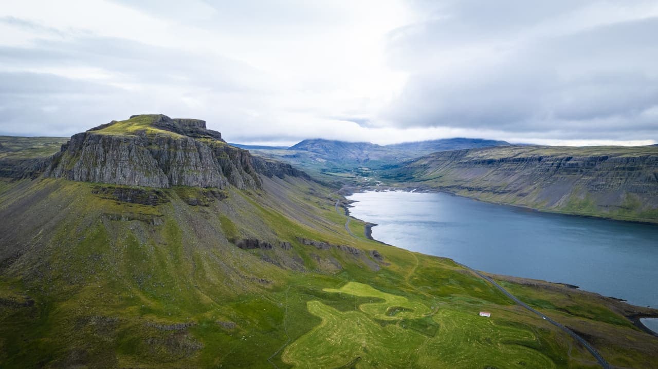 Wide view over Hvalfjörður with steep mountains, blue fjord water, and the road below.